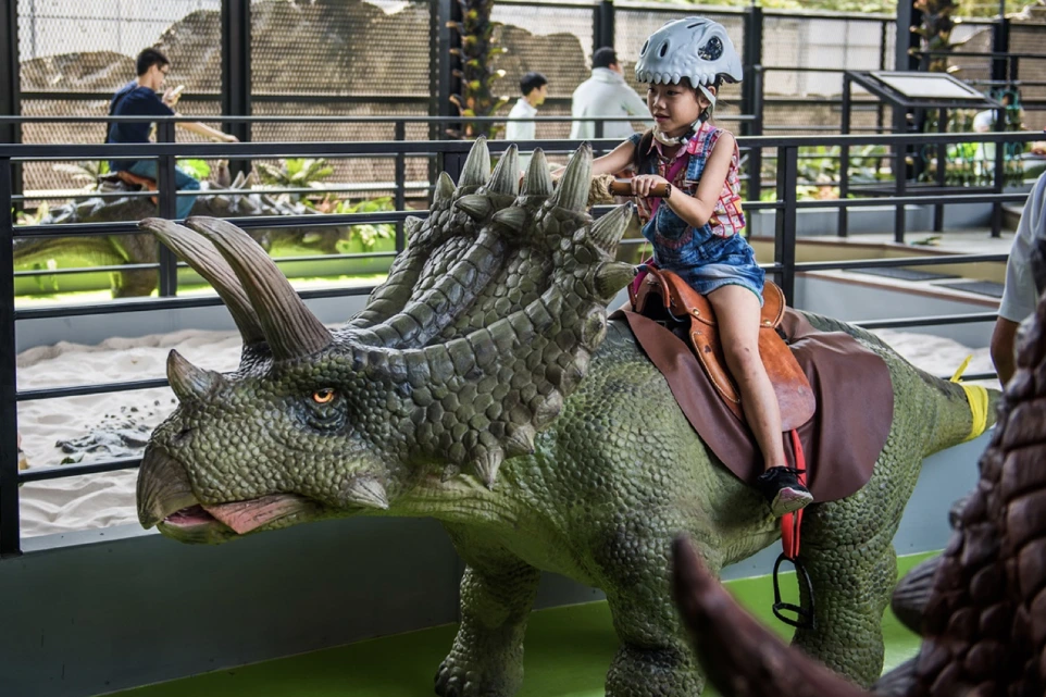 Enfant chevauchant un tricératops grandeur nature dans une installation immersive – Prehistoric Safari