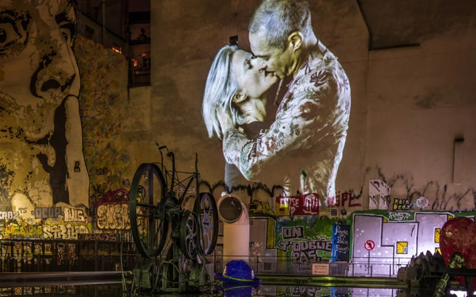 Couple enlacé projeté sur un mur urbain recouvert de graffitis – Le Baiser, art numérique dans la ville