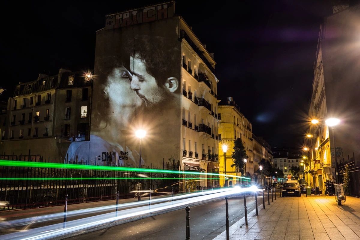 Projection monumentale d’un baiser sur une façade parisienne avec traînées de lumière urbaine – Le Baiser, video-mapping