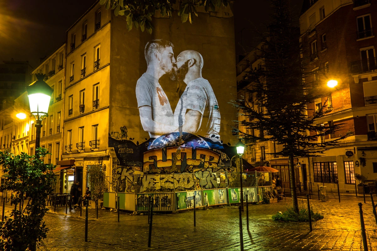 Couple s’embrassant projeté sur un immeuble au cœur d’une place parisienne nocturne – Le Baiser, art dans l’espace public